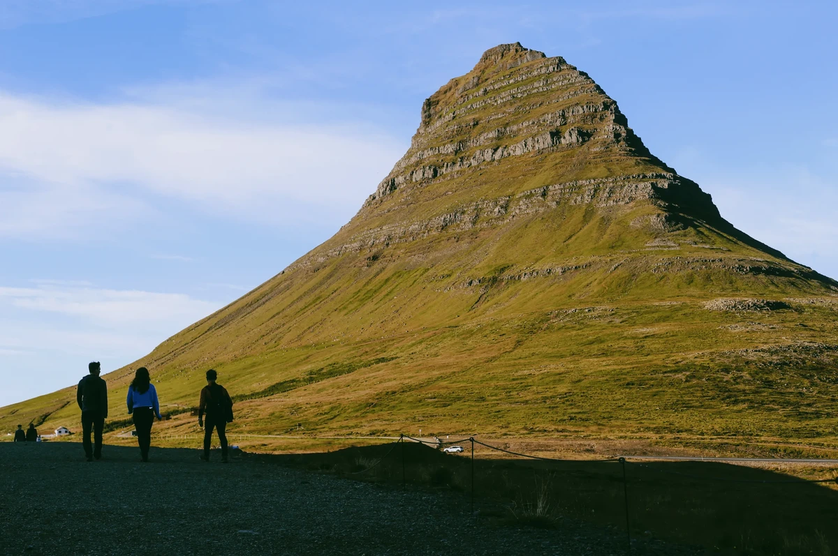 Góra Kirkjufell na Islandii z dwoma turystami podziwiającymi krajobraz w słoneczny dzień