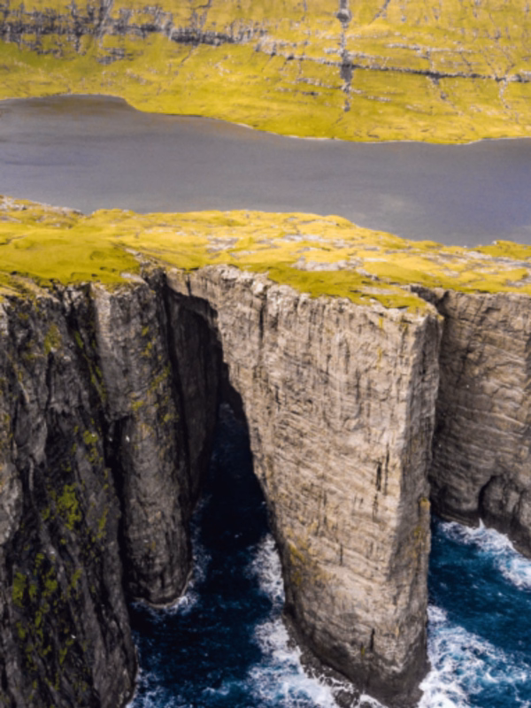Wysokie klify nad oceanem z zielonymi łąkami i jeziorem w tle na wyspach Faroe