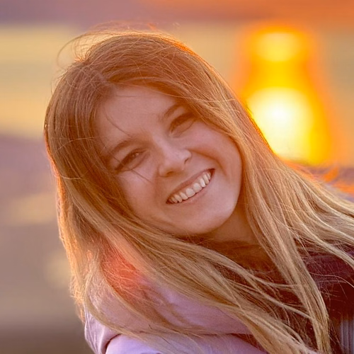 Uśmiechnięta młoda kobieta na tle zachodzącego słońca podczas letniego wieczoru nad wodą