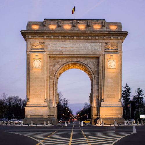 Łuk triumfalny w Bukareszcie oświetlony wieczorem na tle zachodzącego nieba